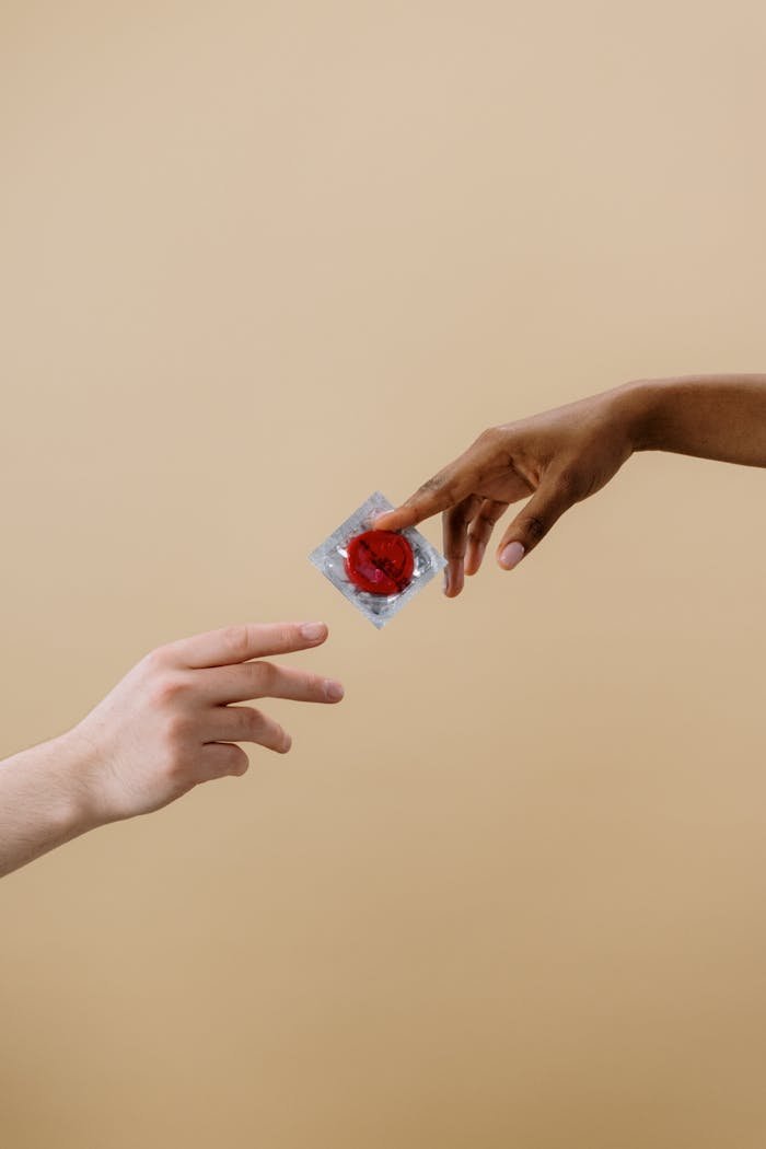Two hands exchange a red condom, promoting safe sex and contraceptive awareness.